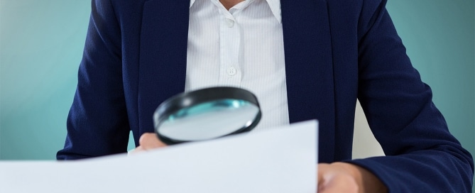 Forensic document examiner reviewing documents with magnifying glass to verify authenticity.