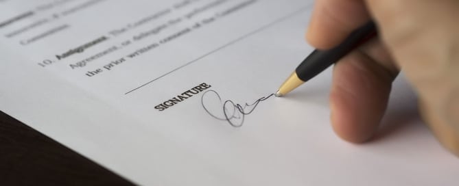 Signing a legal document, representing the importance of working with a forensic document examiner for signature verification and handwriting analysis.