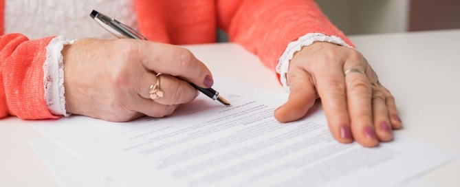 Elderly person signing legal documents, illustrating risks of exploitation through document and signature forgery.