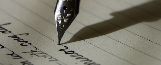 Fountain pen with silver nib writing cursive on a lined sheet of paper.