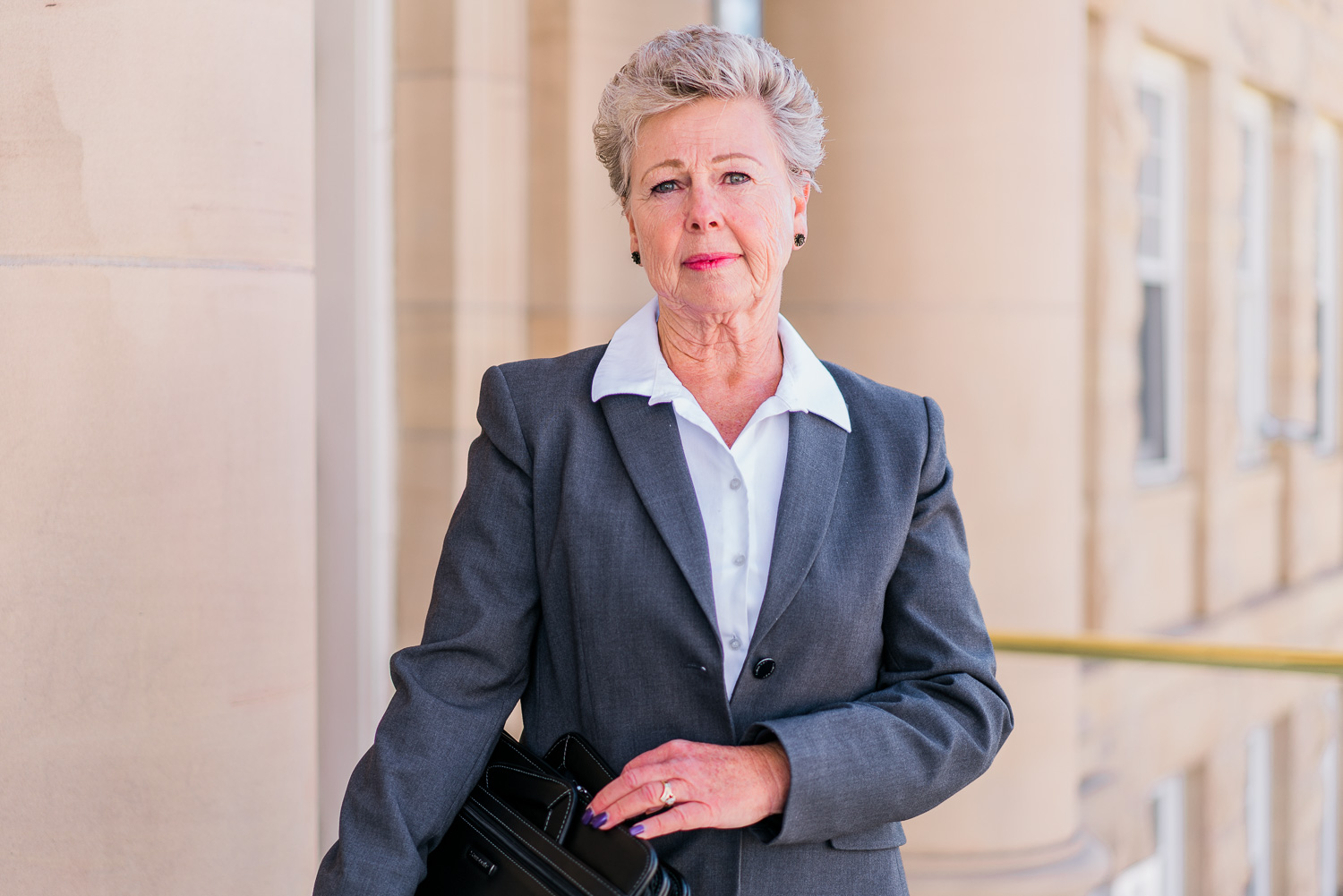 Kathy Carlson, CFDE, CQDE, certified forensic document examiner and expert witness, standing outside courthouse with briefcase.